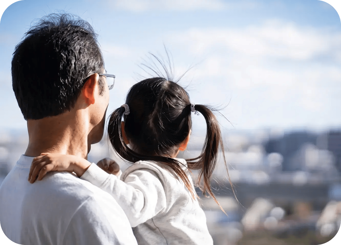 屋外で男性が子どもを抱きかかえながら、親子で景色を眺めている後ろ姿